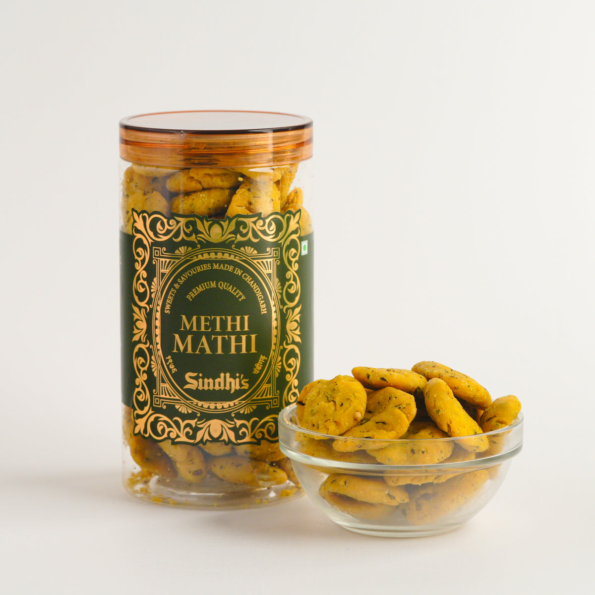 Jar and bowl of Methi Mathi snacks with a decorative label on a white background