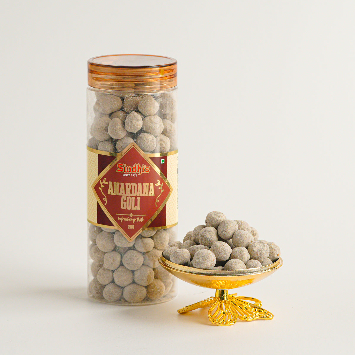 Jar of 'Amarjana Goli' with a decorative bowl filled with the product on a white background