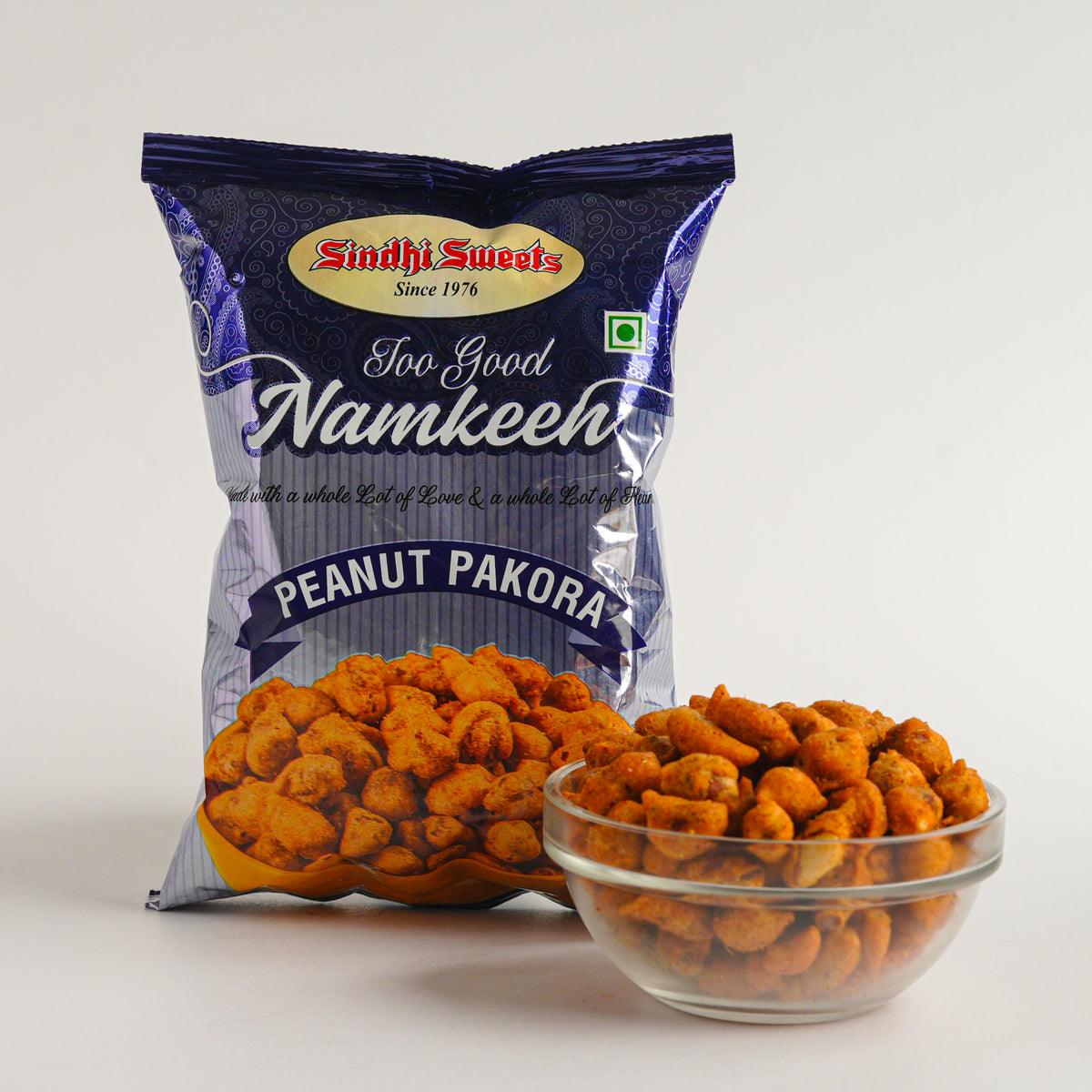 Packaged peanut pakora with a bowl of snacks on a white background