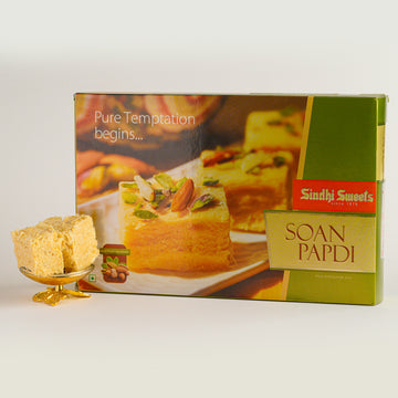 Box of Sindhi Sweets Soan Papdi with a piece of the dessert on a white background