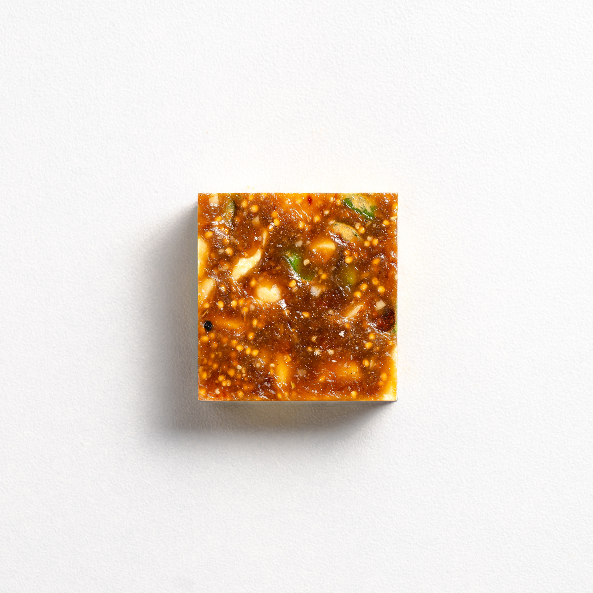 Square piece of food with a glossy sauce on a white background