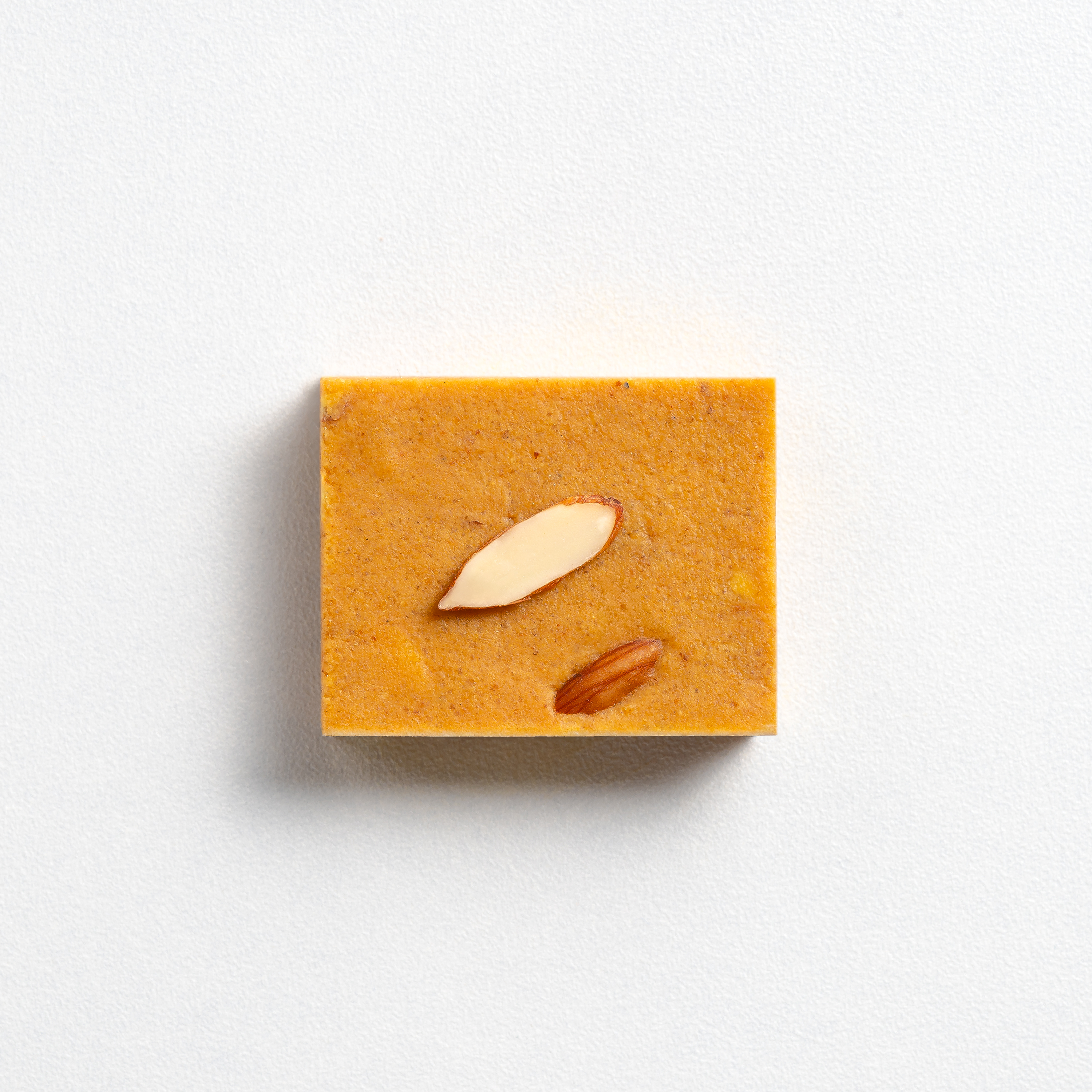 Square bar of orange soap with almonds on a white background