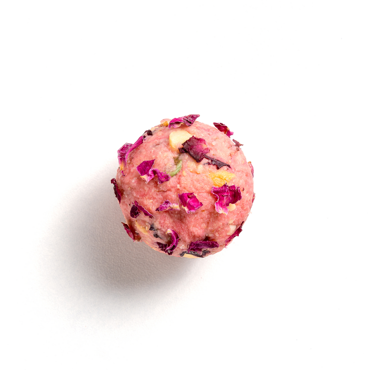 Pink spherical bath bomb with dried flowers on a white background