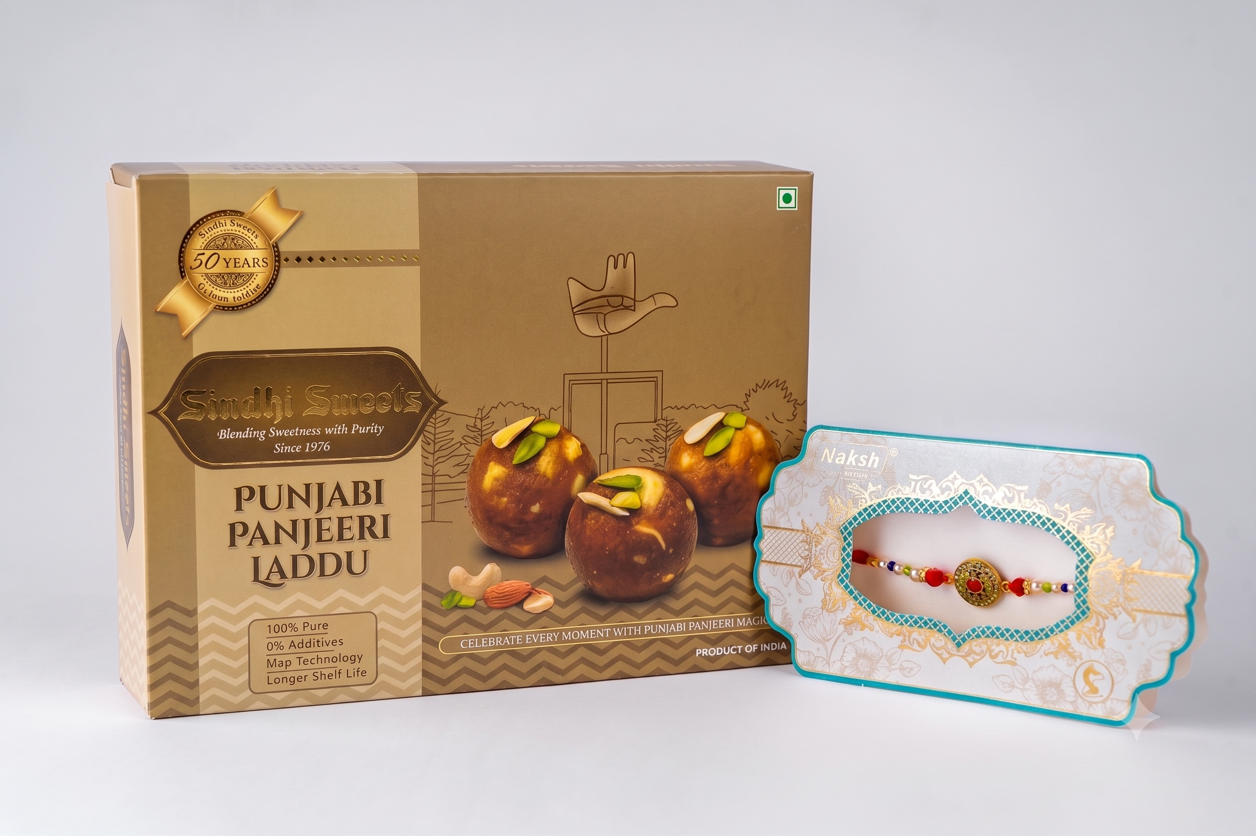 A boxed gift set of Punjabi Panjeeri Laddu sweets next to a packaged rakhi with a decorative thread and a small laddu, photographed on a clean light gray studio background.