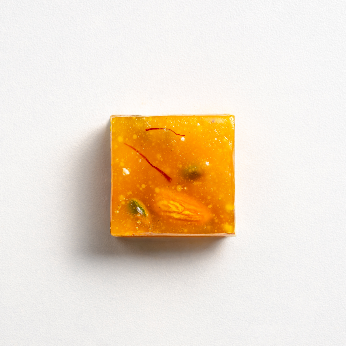 Square piece of amber-colored soap with natural elements on a white background