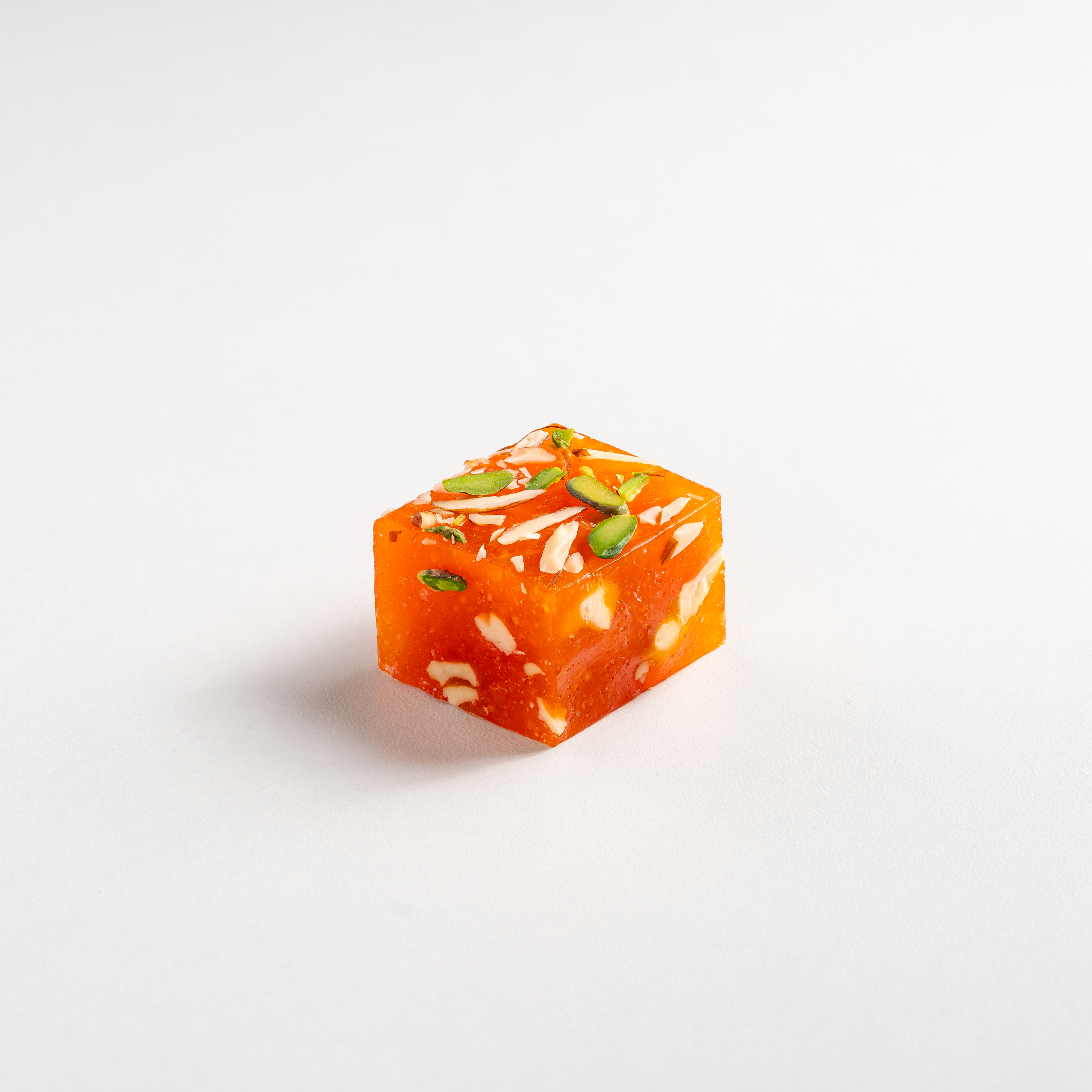 Square piece of orange dessert with white and green toppings on a white background
